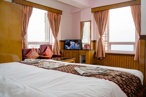 A hotel room with a large bed, a television, a desk with a chair, and a window with curtains. - Doma Residency (Gangtok)
