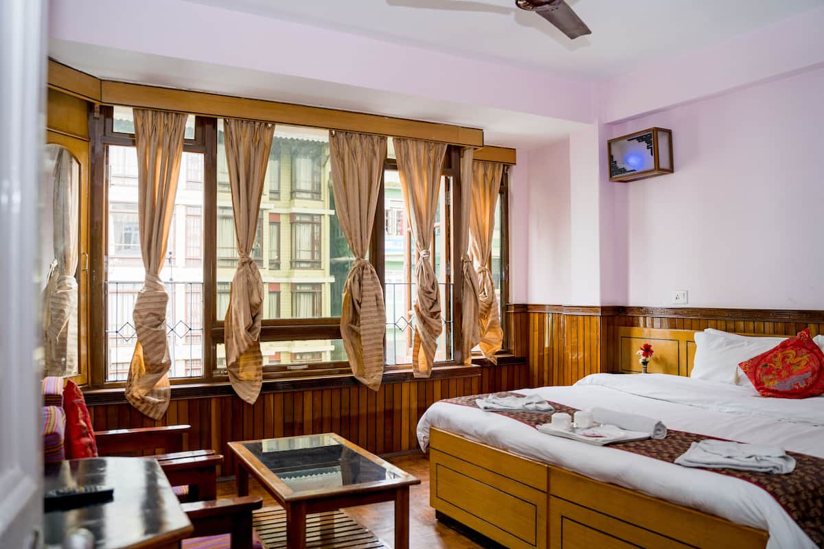 Habitación de hotel con cama, cabecera de madera, una mesita y ventana con cortinas.