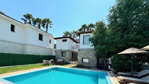 A swimming pool with a tiled edge, lounge chairs, and a stone wall. - Villa Merry - Dalyan Stonehouse with Palmtrees (Muğla)