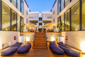 Un hall d’hôtel moderne avec un escalier central, un plancher en bois et des espaces de détente aux couleurs violettes.