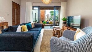 A modern living room with a sofa, a patterned armchair, a TV, and a large window with a view of the outdoors. - Immaculate 2-bed Apartment in Pereybere Grand Baie (Grand-Baie)