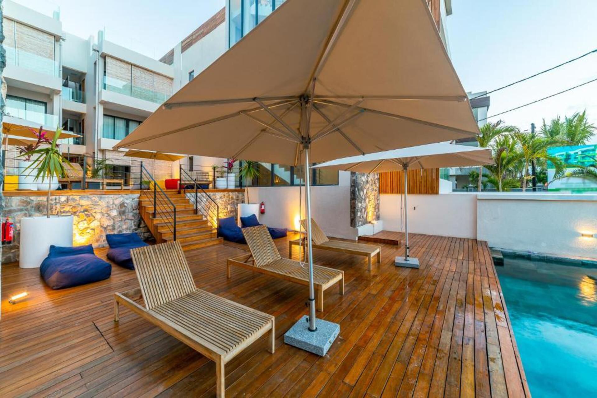 A wooden deck with lounge chairs and a large umbrella, overlooking a swimming pool.