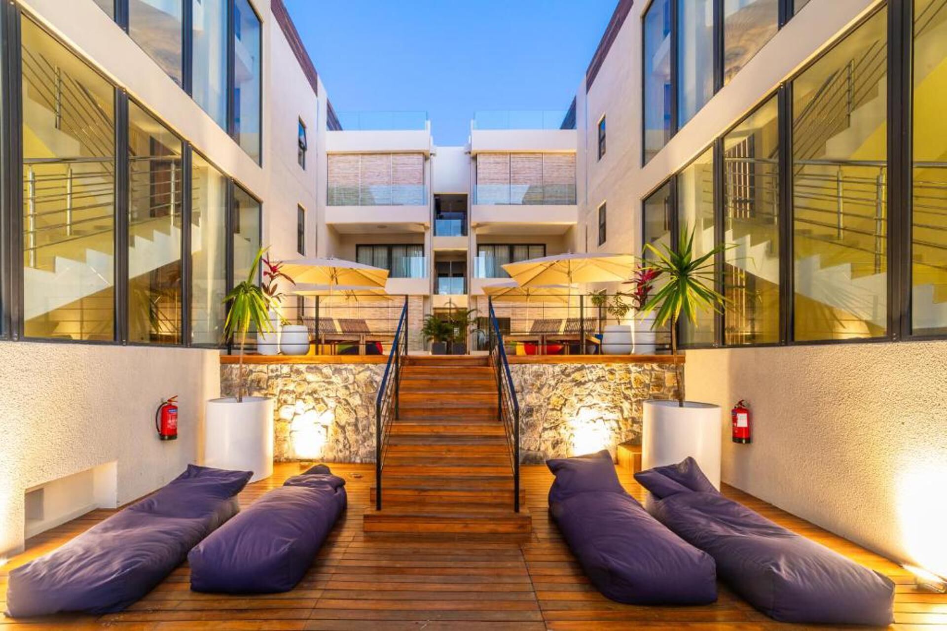 A modern hotel lobby with a central staircase, wooden flooring, and purple seating areas.