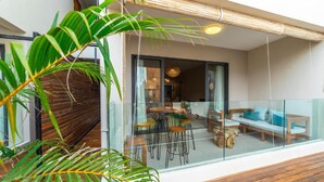 A modern outdoor seating area with a glass balustrade, wooden deck, and tropical plants. - Immaculate 2-bed Apartment in Pereybere Grand Baie (Grand-Baie)