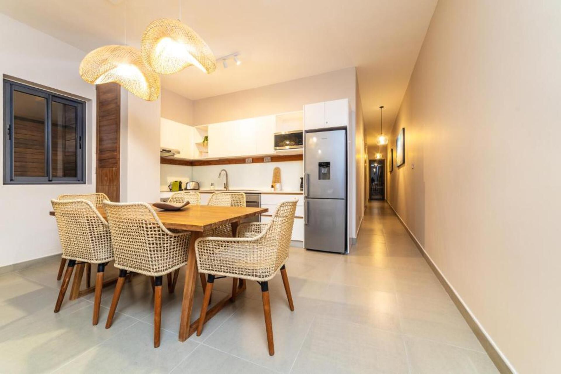 Une cuisine moderne avec un coin repas, comprenant des chaises en osier, une table en bois et un réfrigérateur en acier inoxydable.