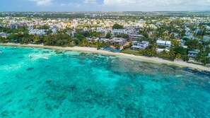 Experience the charm of a coastal town with modern homes and apartments, situated closely along the beach with palm trees and clear waters.