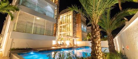 A modern building with a swimming pool, surrounded by palm trees and plants.