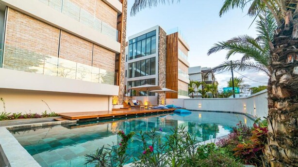 A modern pool area with a clear pool, surrounded by lush greenery and palm trees. - Immaculate 2-bed Apartment in Pereybere Grand Baie (Grand-Baie)