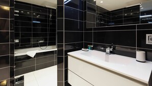 Een moderne badkamer met zwarte tegels, een wit wastafelmeubel en een spiegel.