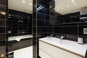 Un baño moderno con azulejos negros, un lavamanos blanco y un espejo.