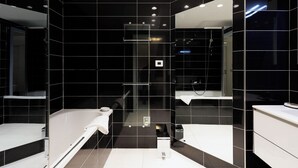 Een moderne badkamer met zwarte tegels, een glazen douchecabine en een wit bad.