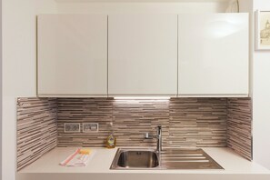 A modern kitchen with a stainless steel sink, wooden backsplash, and white cabinets.