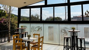 An indoor patio area with a view of the sky and distant buildings, featuring wooden and metal chairs, a tiled floor, and a decorative wall with etched designs. - Smart Accomodation Rhodes by GHH (Rhodes)