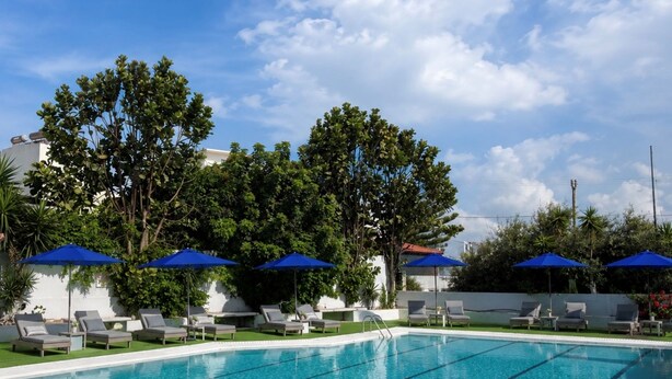 A swimming pool with lounge chairs and umbrellas, surrounded by greenery and a clear sky. - Smart Accomodation Rhodes by GHH (Rhodes)