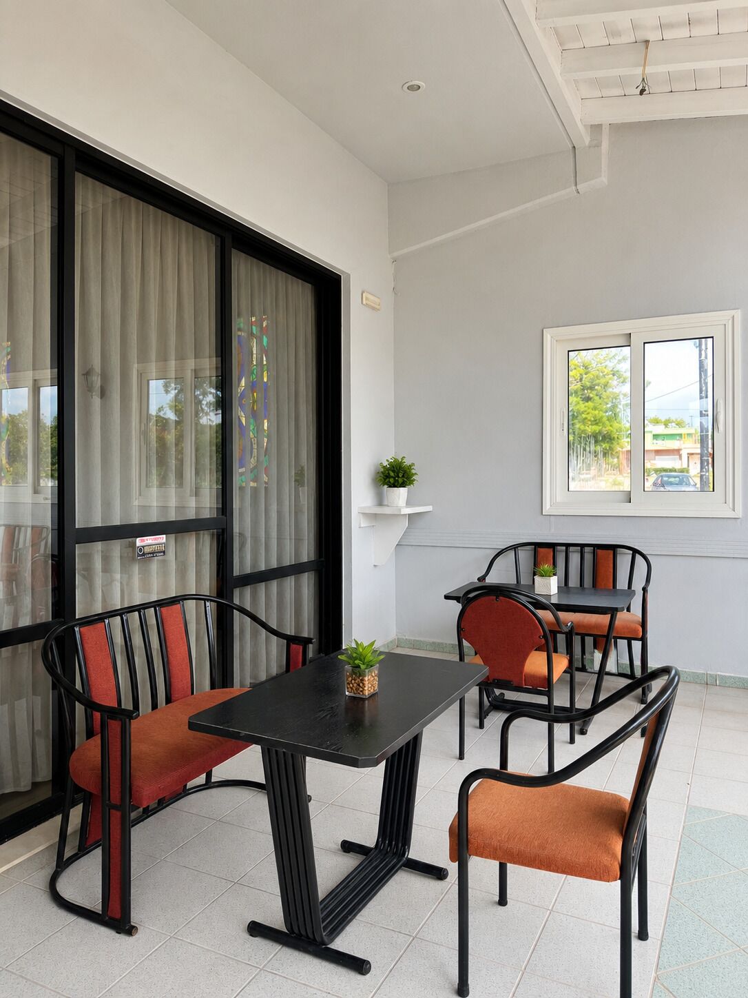 Une pièce avec une table noire et quatre chaises, une plante en pot et une fenêtre donnant sur des immeubles et des arbres.
