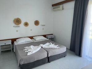Et hotelværelse med to senge, et natbord, en vægmonteret aircondition og et vindue med gardiner.
