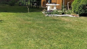 Eine Holzhütte mit Ziegeldach, umgeben von einem gepflegten Rasen und diversen Pflanzen.