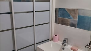 Ein Badezimmer mit einem weißen Waschbecken, einem Spiegel, einem Handtuch und einer Duschkabine mit Milchglas-Türen.