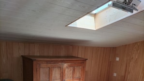 Ein Zimmer mit schrägen Wänden, Holzwandverkleidung, einem großen Schrank, einem Bett mit grüner Decke und einem Dachfenster.