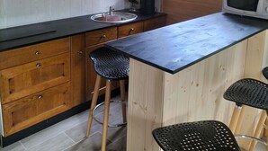 Eine kompakte Küche mit Holdekor-Schränken, einer schwarzen Arbeitsplatte, einem Spülbecken, einer Mikrowelle und zwei schwarzen Stühlen.