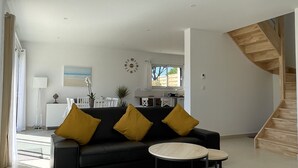 Una sala de estar moderna con un sofá negro, dos cojines amarillos, una mesa de centro redonda y una escalera a la derecha.