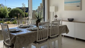 Comedor con una mesa preparada para cuatro personas, sillas blancas, una planta en maceta y un cuadro en la pared.