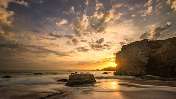 Un atardecer sobre una costa rocosa con olas suaves lamiendo la orilla.