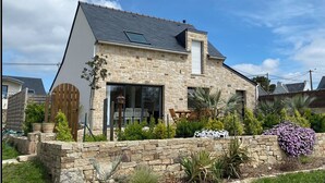 Una casa de piedra con techo inclinado, ventanas amplias y un muro de piedra con plantas.