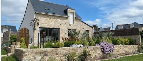 A stone house with a sloped roof, large windows, and a stone wall with plants.