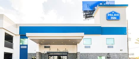 Una entrada de hotel moderna con una decoración azul y blanca, un vestíbulo cubierto y un letrero que indica que es un Palace Inn.