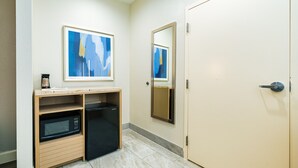 A compact kitchenette with a microwave, refrigerator, and wooden shelves. There are two framed abstract paintings on the wall. - Palace Inn IAH Houston Bush Intercontinental Airport (Humble)