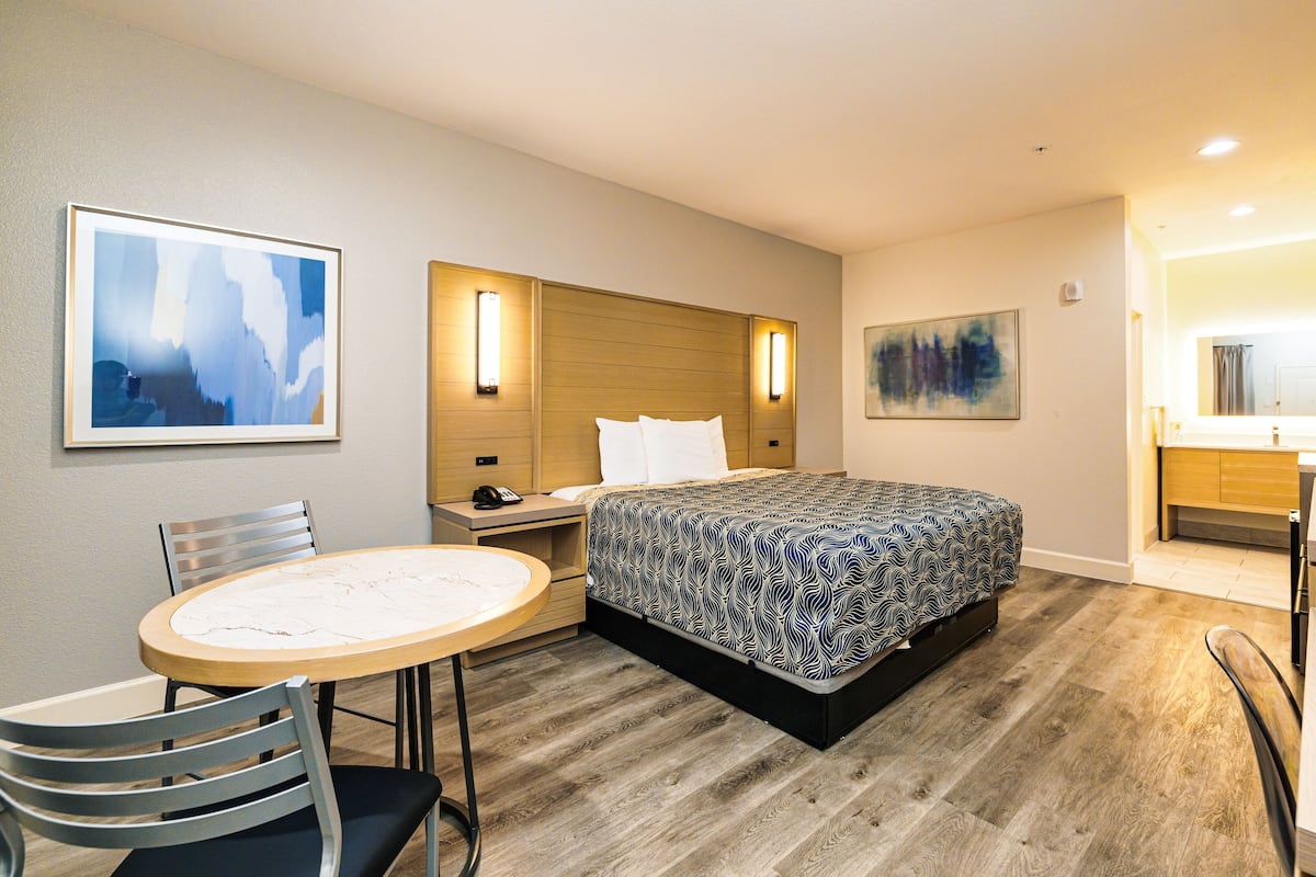 A hotel room with a bed, a desk with a chair, a round table, and two wall-mounted light fixtures.