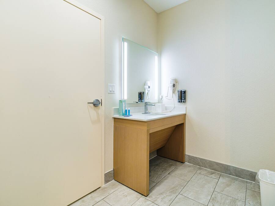 A bathroom with a wooden vanity, a mirror, a hairdryer, and a trash bin.