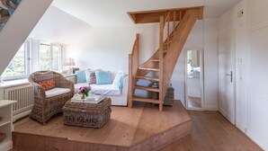 A loft-style bedroom with a wooden staircase, a wicker sofa, a white bed, and a view of the outdoors. - Cozy 3-room apartment on approx. 55 m² for 4 persons. (Wenningstedt-Braderup (Sylt))