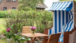 A wicker chair with a blue and white striped canopy, a wooden table, and a vase with pink flowers. - Cozy 3-room apartment on approx. 55 m² for 4 persons. (Wenningstedt-Braderup (Sylt))