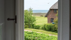 A view through an open door of a house with a brick exterior, a lawn, and a body of water in the background. - Cozy 3-room apartment on approx. 55 m² for 4 persons. (Wenningstedt-Braderup (Sylt))