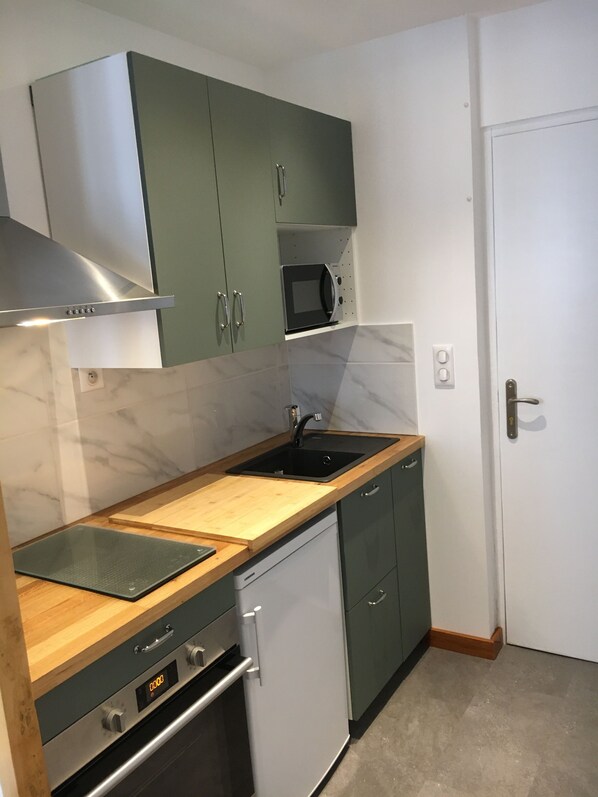 Une cuisine compacte avec des meubles de couleur verte, un four à micro-ondes, un évier, un lave-vaisselle et une cuisinière.