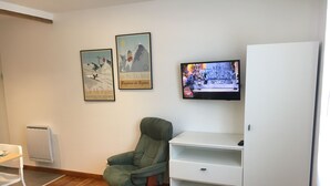 A room with a green chair, a white desk, a TV on the wall, and two framed pictures. - Downtown studio*** with outdoor parking and private, secure bike storage. (Bagnères-de-Bigorre)