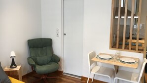 A small, neatly arranged room with a green chair, a white table with plates and glasses, a lamp, and a bed with a yellow cover. - Downtown studio*** with outdoor parking and private, secure bike storage. (Bagnères-de-Bigorre)