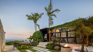 A modern outdoor patio with a stone fire pit, seating area, and a view of the ocean. - Airship Bali by Alex Villas (Pecatu)
