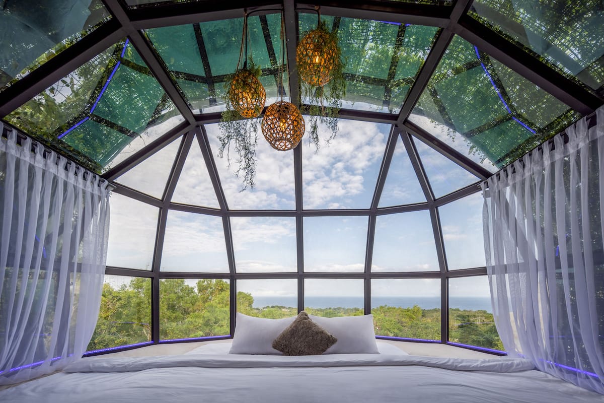 A room with a glass ceiling, a bed with white linens, and a view of the outdoors.