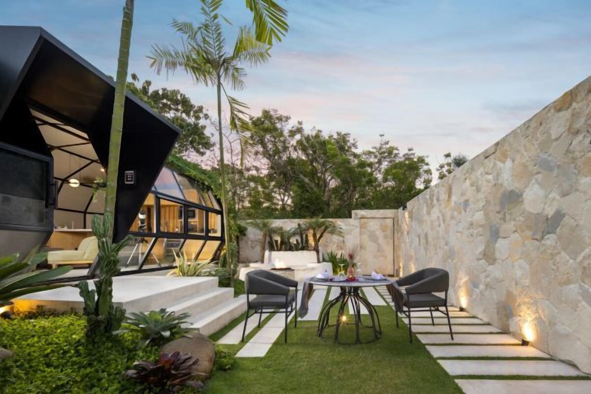 Un patio moderno al aire libre con zona de comedor, escalones que conducen a un área de estar cubierta y una pared de piedra.