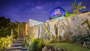 A modern building with a glass dome, surrounded by a landscaped garden with cacti and palm trees, under a starry night sky. - Airship Bali by Alex Villas (Pecatu)