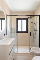 Un baño moderno con ducha de vidrio, un lavamanos blanco y un inodoro.