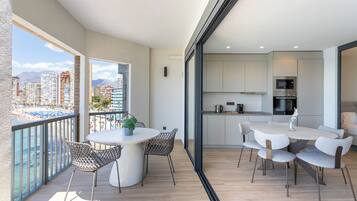 Een modern appartement met balkon en uitzicht op zee, een keuken met moderne apparatuur, en een eethoek met een ronde tafel en stoelen.