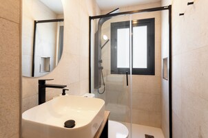 Un baño moderno con ducha de vidrio, lavabo blanco y retrete.