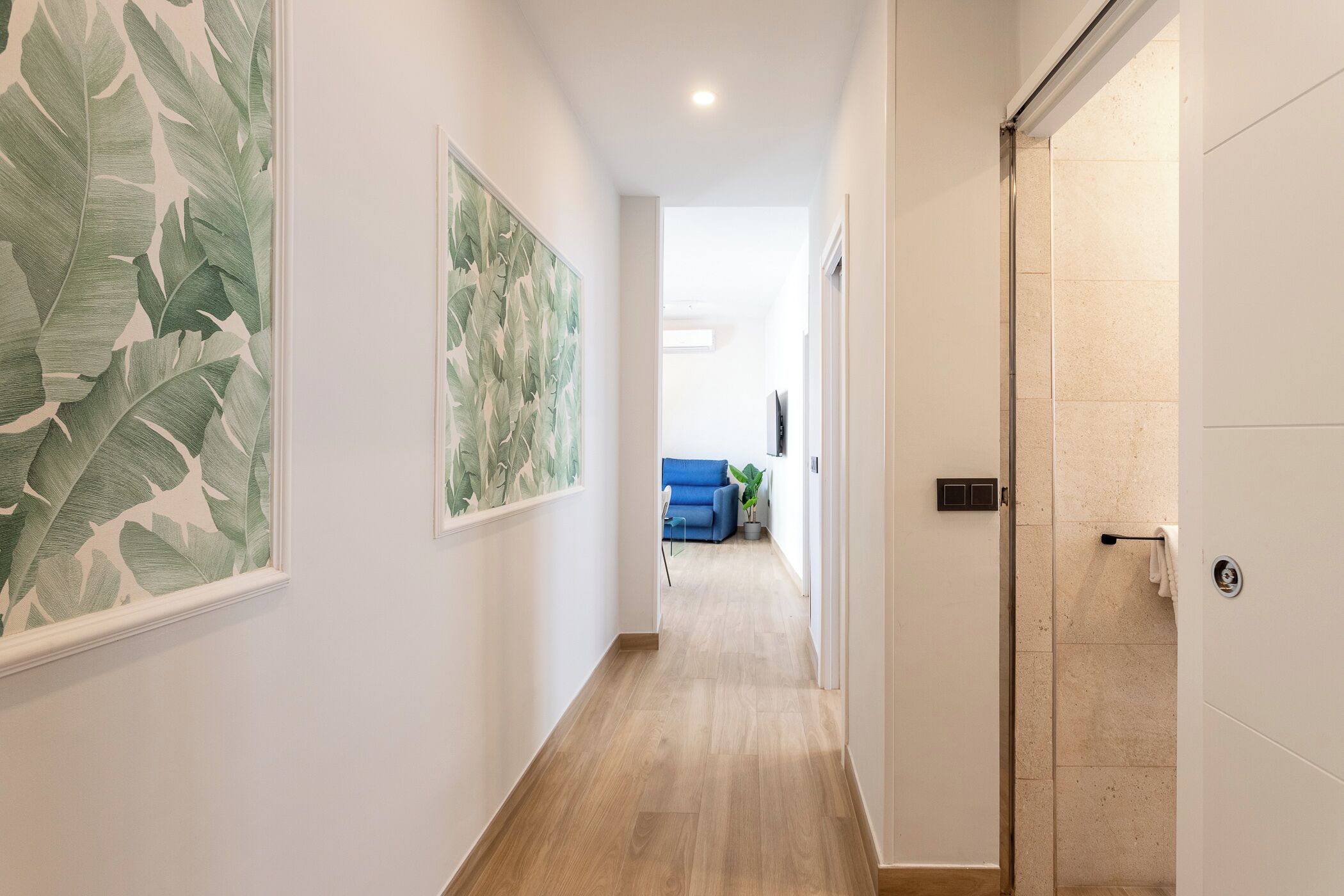 A hallway with a wooden floor, white walls, and large leaf-patterned artwork.