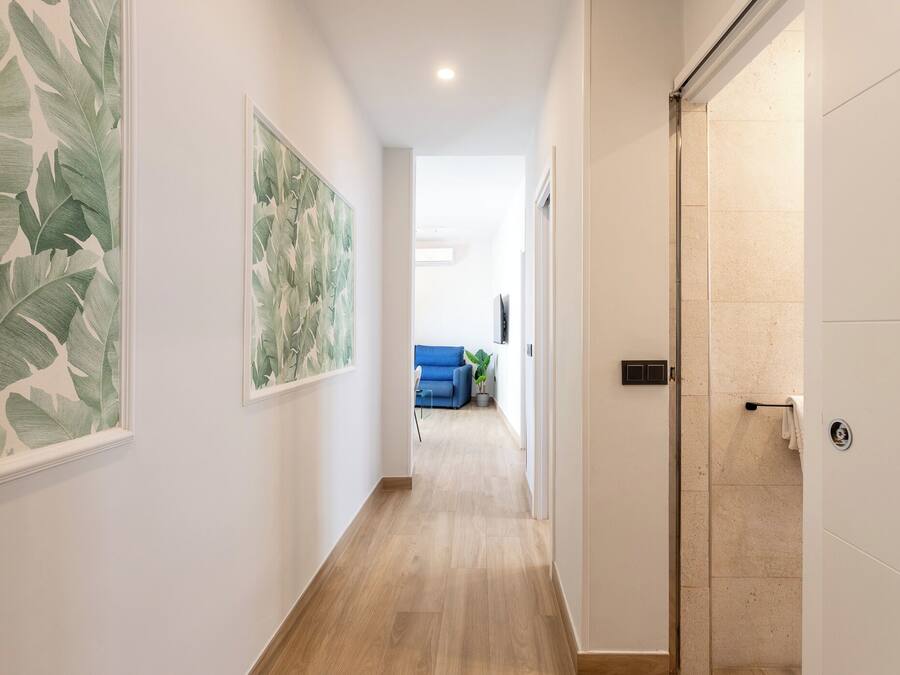 A hallway with a wooden floor, white walls, and large leaf-patterned artwork.