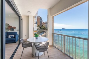 A balcony with a white table and chairs, a blue sofa, and a view of the sea.