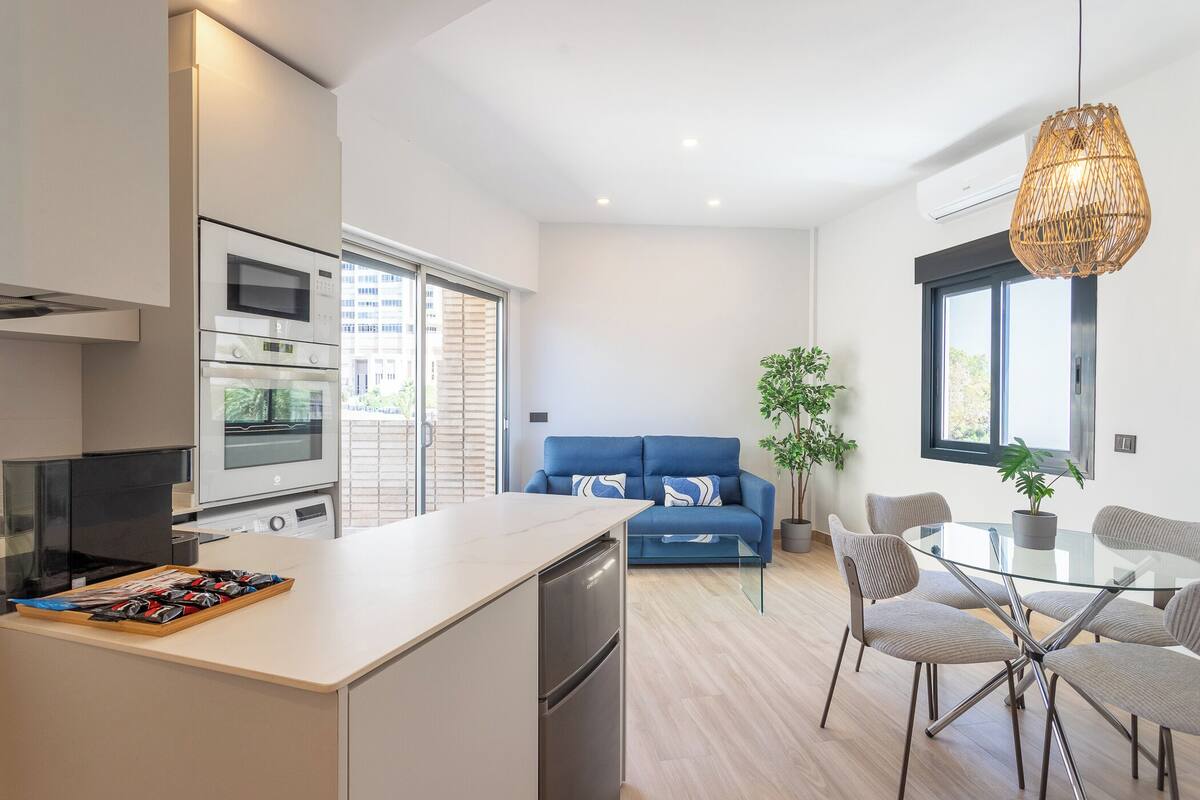 Uma cozinha moderna com área de refeições, um sofá azul e uma mesa de vidro.